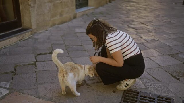 Young woman in lecce, puglia, italy crouching on cobblestone street petting a cat, creating a serene urban scene.