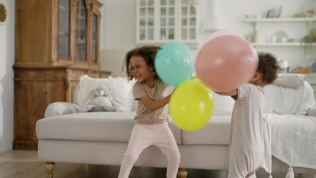 Happy children fighting by balloons, African American siblings having fun. Carefree childhood moments and memories, family concept, children party for Birthday, cute black girl smiling and laughing
