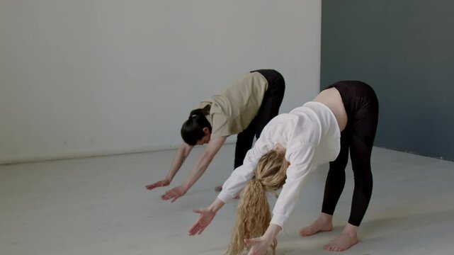 Young male and female dance partners bending forward with straight arms and back then rolling up slowly while doing warmup before rehearsal in studio