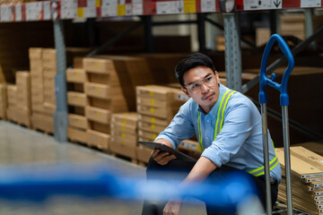 A man in a blue shirt and safety vest sits on a cart in a warehouse. He is holding a tablet in his hand