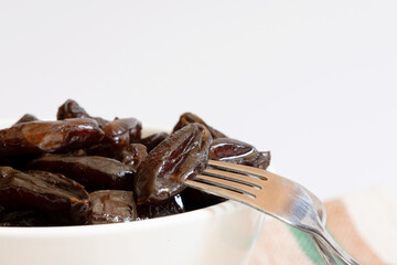 A portion of dates inside a white ceramic bowl photographed up close