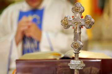 Holy Cross with Jesus Christ on the altar during the Holy Mass, the priest in the background and empty space for text.