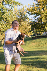Smiling middle-aged man walks and plays with a small dog in public park