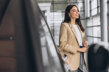 Smiling car seller, businesswoman in beige suit standing in car salon and using tablet for choosing right car.