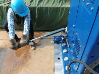 A worker in protective gear using a torque wrench to tighten bolts on heavy machinery. The image captures the precision and physical effort involved in industrial maintenance and mechanical engineerin