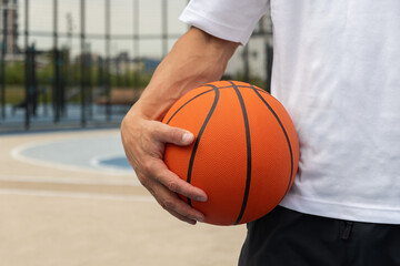 Sporty man holding orange basketball ball on sports court. Focus on ball. Close up. Basketball coach. Copy space.