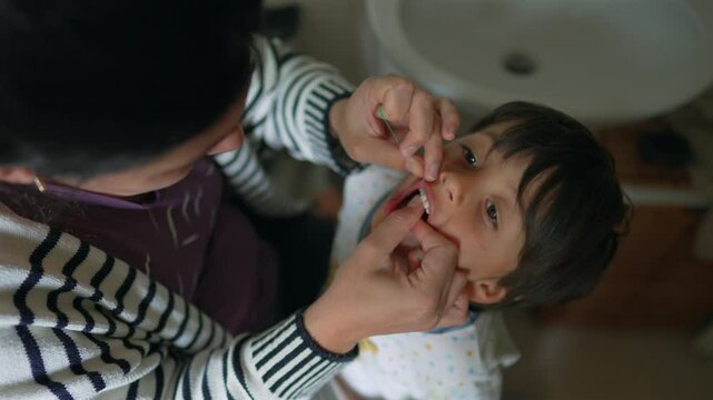 Overhead view of mother flossing toddler&rsquo;s teeth in a bathroom, emphasizing hygiene and attentive care. a daily dental routine within the family setting