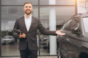 Portrait, smiling man at outside car dealership for car sale in a commercial parking. Business, luxury and automobile trade with a happy bearded salesman in suit outdoor for transport service