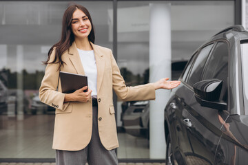 Portrait of confident successful saleswoman in suit with digital tablet in hands standing in outdoor car dealership