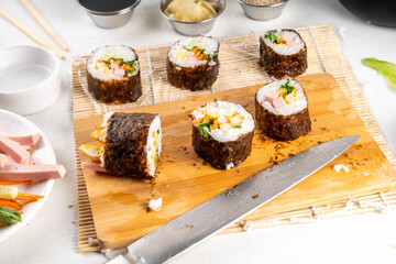 Traditional Korean food kimbap, with ham, vegetables and lettuce. Cooking process, making homemade kimbap, step by step cooking and cutting slicing with hands in pic, top view