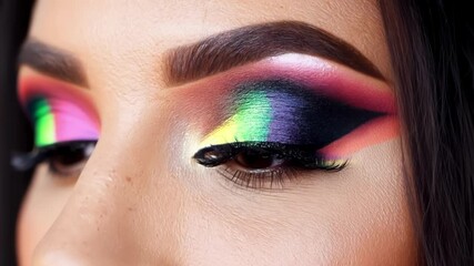 Close up of a woman with bright and colorful eyeshadow in a neon rainbow palette. The makeup artist is showcasing their skills