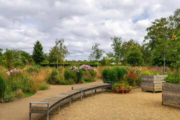 Long curved wooden bench in a park with raised flower beds and gravel path.