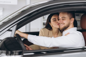 Portrait of smiling beautiful couple sitting in modern luxury car, happy excited young man and woman buying new car in dealership.