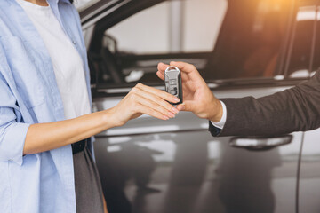 Close-up shot of salesman or manager giving car keys to modern woman new car owner in car dealership