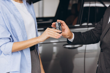 Close-up shot of salesman or manager giving car keys to modern woman new car owner in car dealership