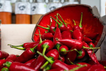 A bowl full of red peppers spread on a table with spices in the background.