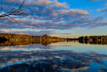 Cloudy sky over autumn forest reflected in the surface of the lake during sunset