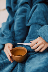 Person wrapped in blue blanket sitting on bed, holding bowl and spoon