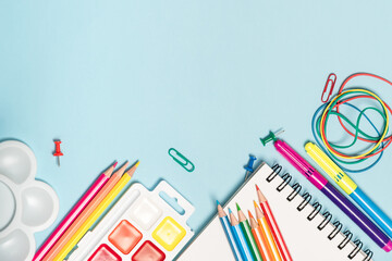 Back to school concept mockup. Colorful school supplies, notepad with iron spring, paints, felt-tip pens and pencils on a blue background.