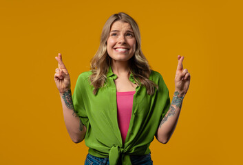 Stylish woman praying with crossed fingers, yellow background.Lady begs someone