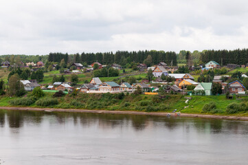 Obraz premium Village with traditional wooden houses on the bank of Sukhona river near Totma town, Vologda region, Russia. Green forest in the distance