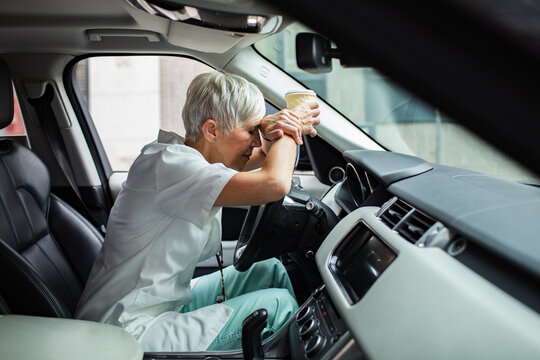 Senior nurse exhausted and stressed in car holding coffee cup