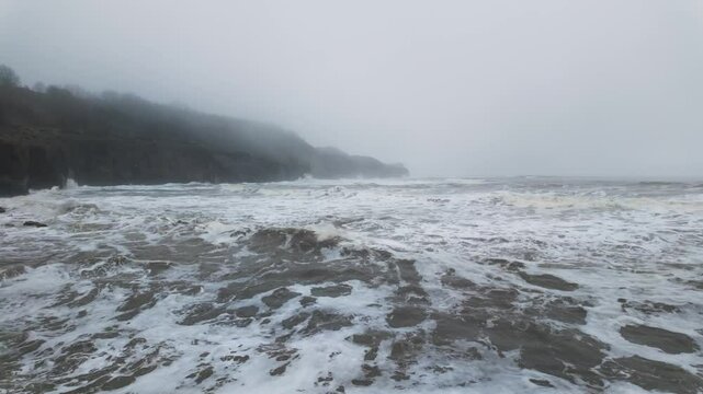 Very mist and foggy scene on the coast of the UK. Winters coastal seascape with small boats and rough seas crashing against the rocks and cliffs on the east coast of the UK. English cold spell