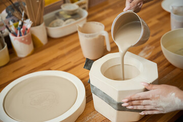 Close up of female hands pouring pottery mixture into mold for mug