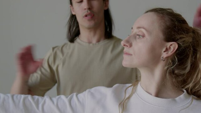 Young woman holding arm outstretched and keeping good posture under guidance of male choreographer during dance class in studio