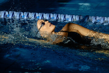 Female athlete swims with a back stroke. Splashes of water scatter in different directions