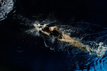 Female athlete swims with a back stroke. Splashes of water scatter in different directions