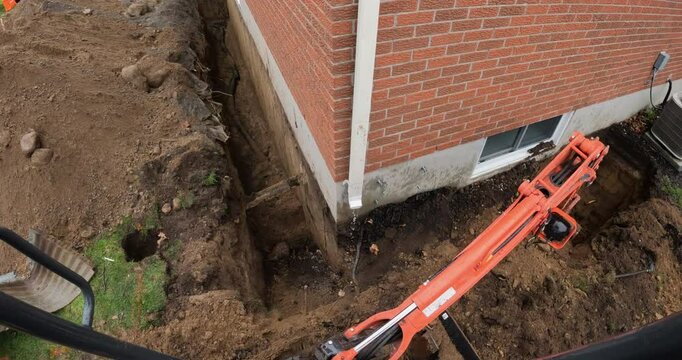 Mini Excavator carefully digging out house foundation to repair leaks - first person view of construction operator