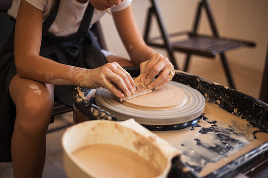 Girl is using a pottery scrapper to smooth the edges of a clay p