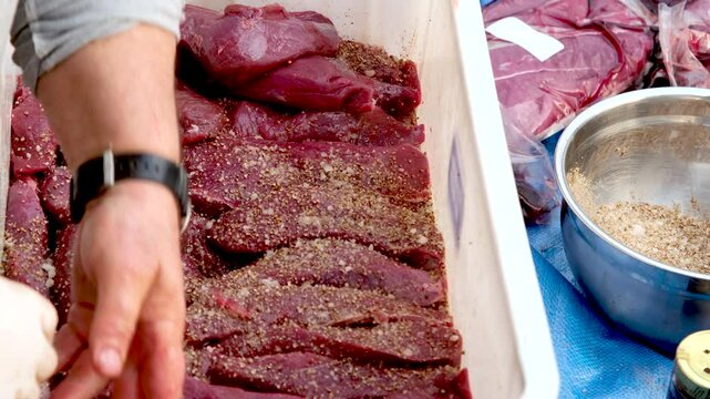 Man stacks pieces of prime venison meat to spice and cure, biltong process