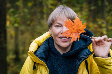 Smiling blonde woman covering eye with autumn leaf