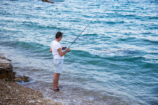Fisherman by the waves with fishing rod looking at mobile phone