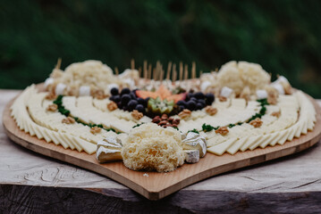 Heart-shaped wooden board with various cheeses and garnishes