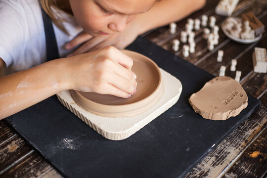 Girl is using a clay stamp to engrave letters and ornaments on a