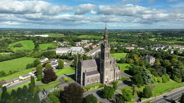 St. Macartan's Cathedral, County Monaghan, Ireland, September 2022. Drone orbits clockwise while pushing closer to the Roman Catholic architecture with a road and vehicles on a bright sunny afternoon.