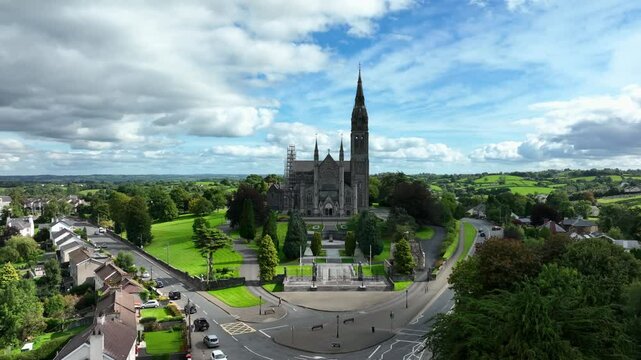 St. Macartan's Cathedral, County Monaghan, Ireland, September 2022. Drone pushes forward over the Roman Catholic architecture above green gardens and busy roads under cloudy blue sky.