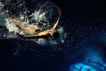 Female athlete swims with a butterfly style. Splashes of water scatter in different directions
