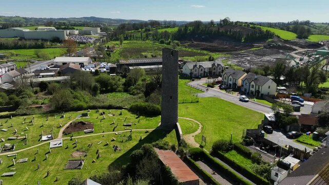 Round Tower, Clones Town, County Monaghan, Ireland, April 2023. Drone orbits the Monastic 10th Century building clockwise with the old cemetery and Cassandra Hand Heritage Centre in the background.
