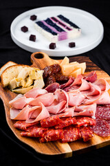 Banquet meat board with slices of sausage, ham, parmesan, gouda, sun-dried tomatoes, bread and piece of cake.