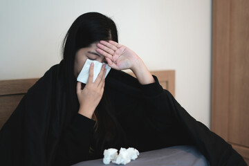 An asian young woman caught cold, sneezing into tissue, also having a headache and fever caused of Virus, infection, taking Medicines with warm water on bed and lying on bed, stressed and depression.
