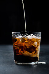 Cocktail White Russian in a glass with pouring cream.