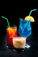 Set of alcoholic cocktails Tequila Sunrise, Blue Lagoon and White Russian on a dark background.