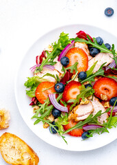 Strawberry and chicken fresh salad with arugula, blueberries, onion and walnuts, white background, top view