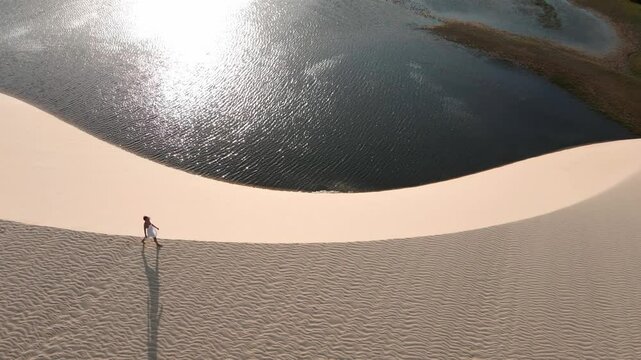 Pessoa andando nas dunas no por do sol com imagem de drone