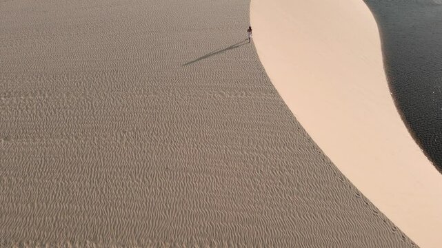 Pessoa andando nas dunas no por do sol com imagem de drone