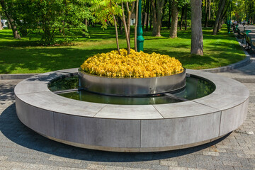 Modern round bench with flowerbed and water in city garden or park. Kharkiv city, Ukraine. Big...